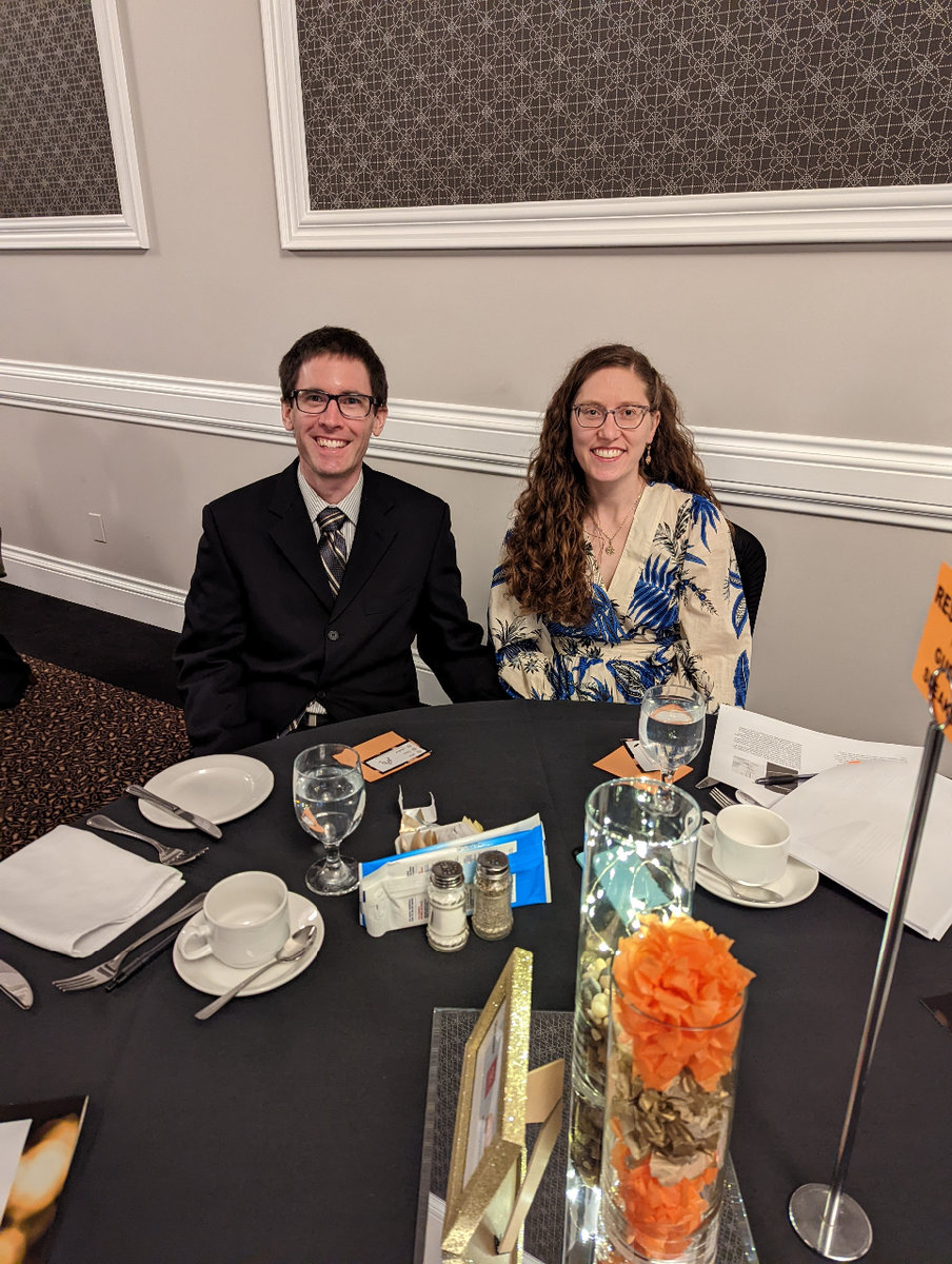 A well dressed couple seated at a circular banquet table smiling towards the camera.